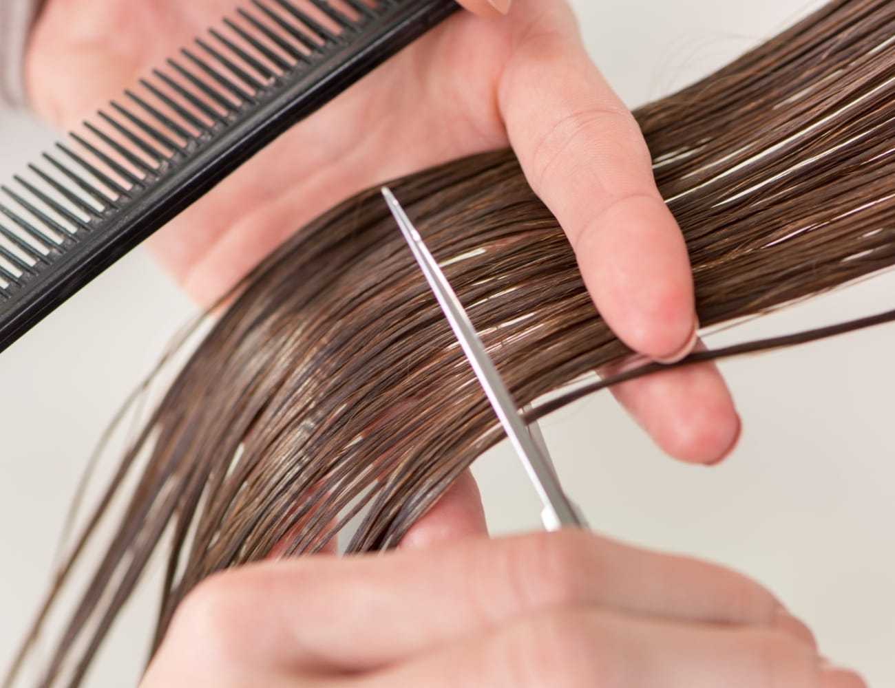 Haircut in progress with comb and scissors on brown hair.